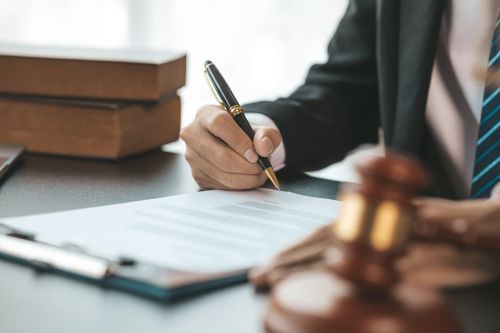 A lawyer sits in his office, on a table with a small hammer to beat the judges desk in court. and justice scales, lawyers are drafting a contract for the client to use with the defendant to sign.