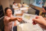 Woman receiving tax refund check from government in office, focus on check, blurred background suitable for copy space.